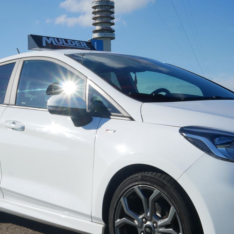 Zijkant van de Ford Fiesta ST-Line lesauto met het Mulder-lesbord en de zendmast van IJsselstein